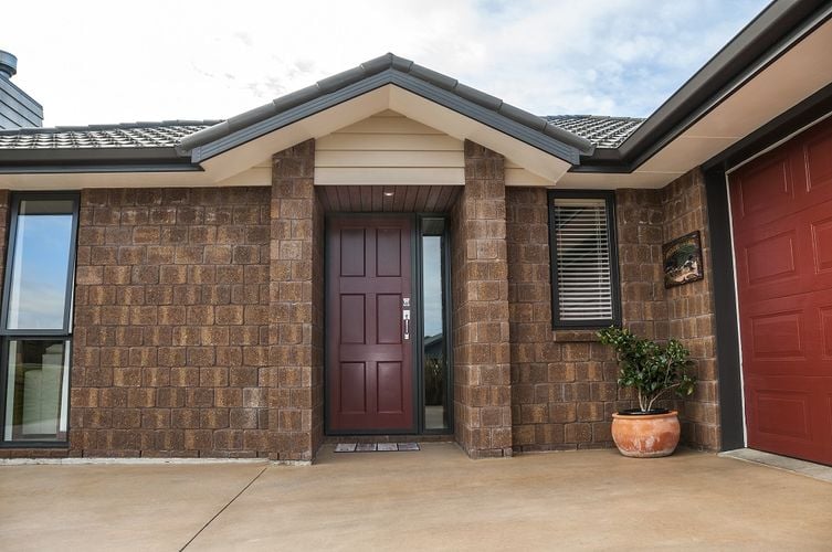 Exterior of a townhouse with dark brown bricks and a dark red front door.