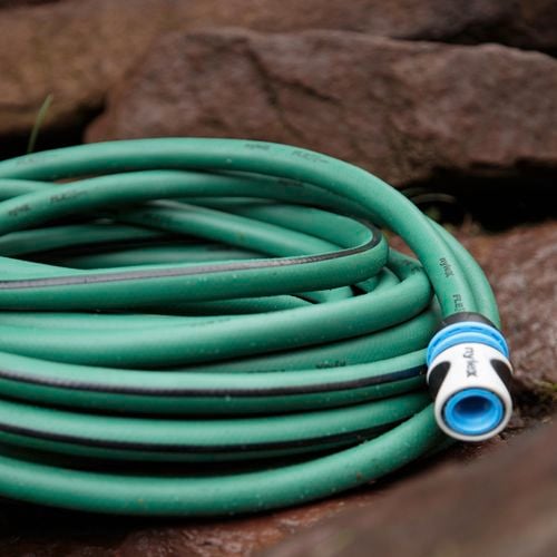 Green Nylex garden hose with a tap fitting fitted on end sits coiled on some garden paving rocks
