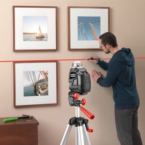 Man marks a line with a pencil on wall to hang picture frame. Ozito laser level is projecting a straight guideline to follow