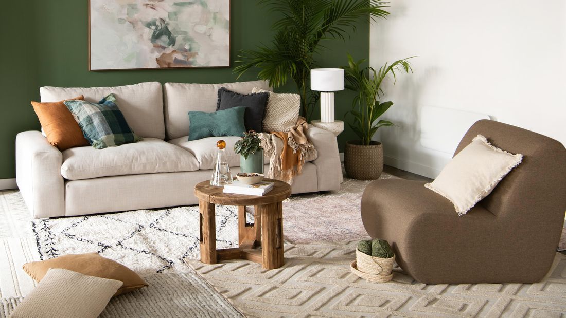Layered interior rugs in a living room featuring a calming green feature wall and warm brown toned furniture.