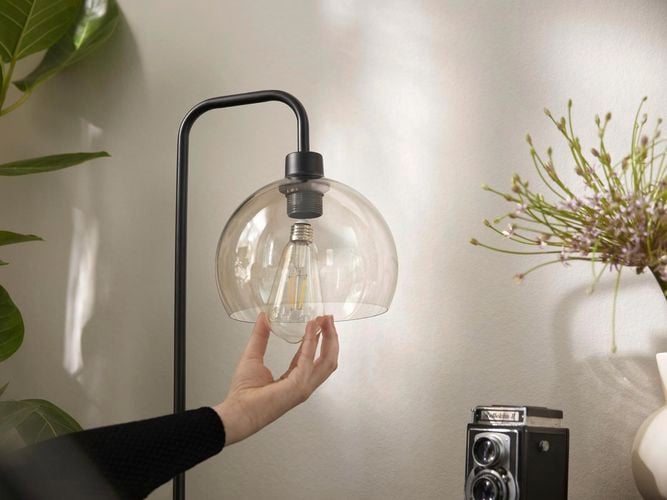 A person screwing in a light globe into a floor lamp
