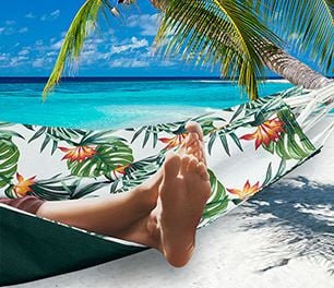 A pair of bare feet hanging out of a hammock on a tropical island