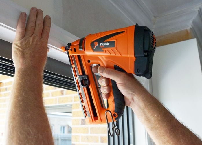 Person nailing door frame to wall using nail gun