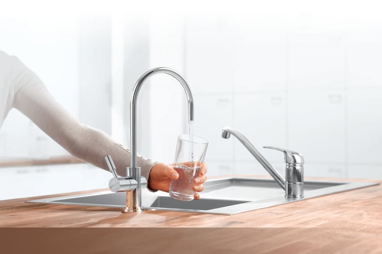 Person filling glass with water from stainless steel tap