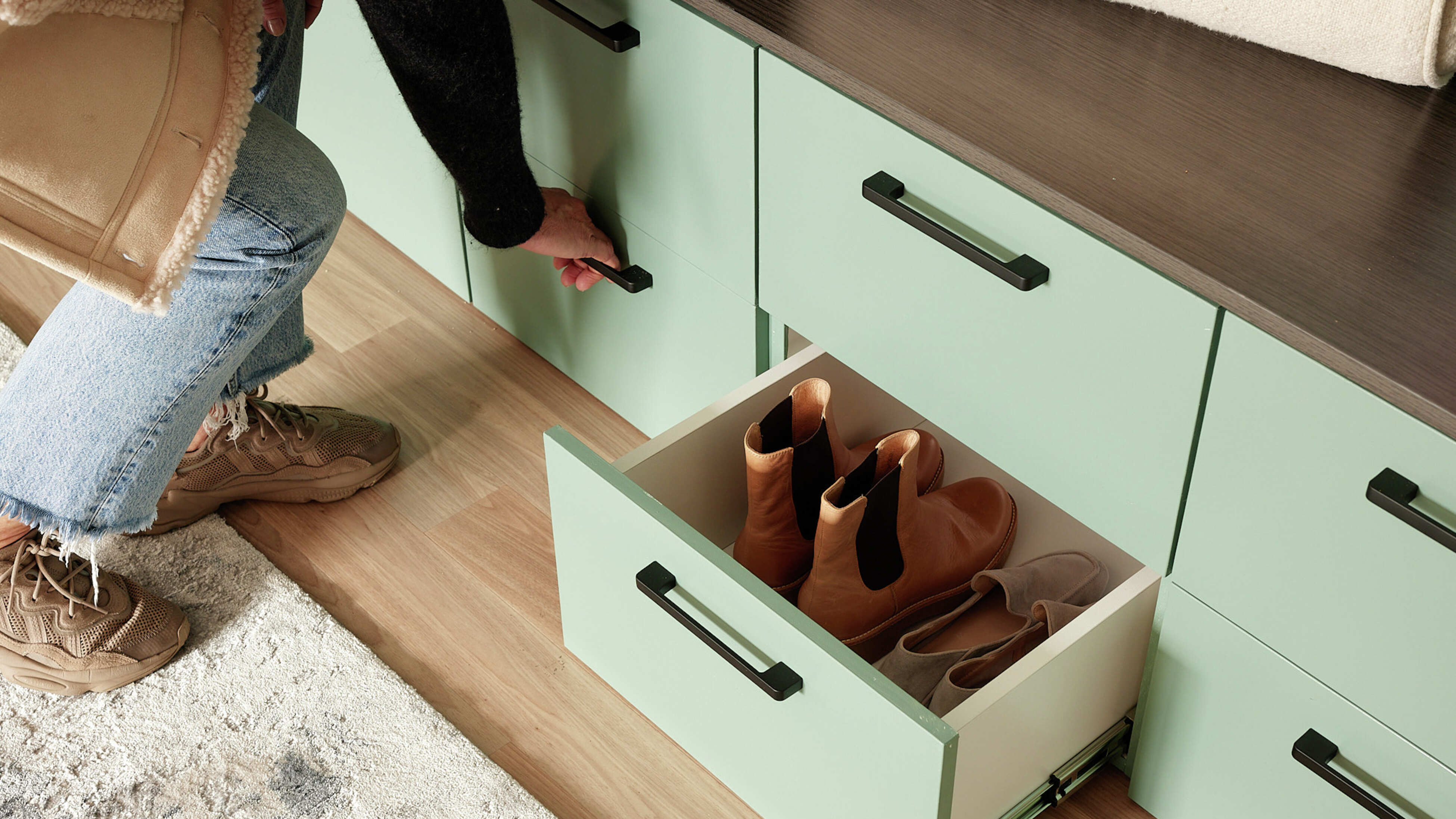 Shoe drawer open with shoes inside and person holding drawer handle.