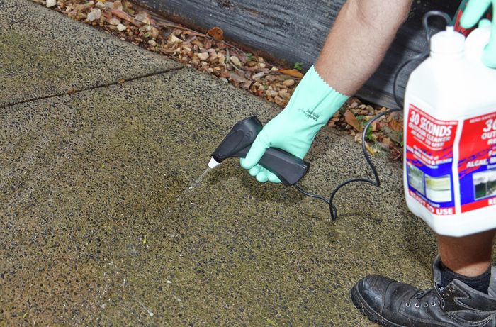 A person wearing protective gear spraying chemical cleaner on a driveway
