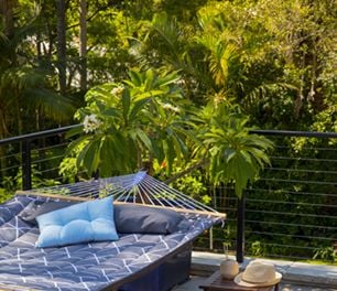 A padded freestanding hammock with cushions in front of a potted plant on a balcony