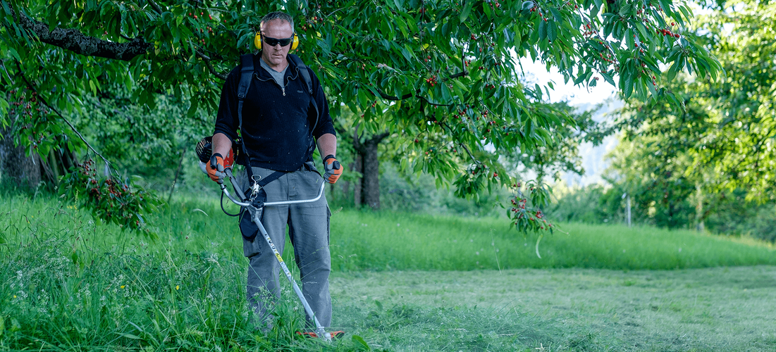 Person trimming grass with harnessed snipper