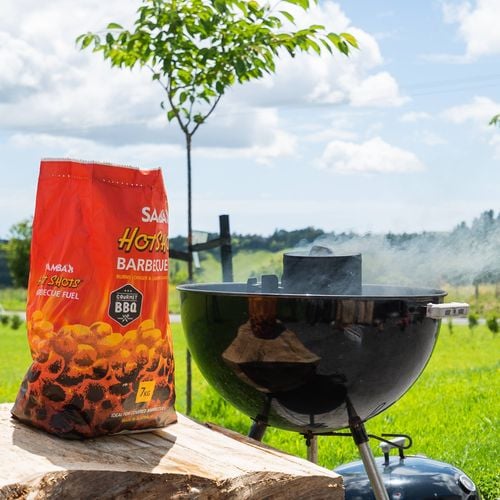 Kettle barbecue smoking behind a bag of Samba 'Hot Shots Barbecue Fuel'