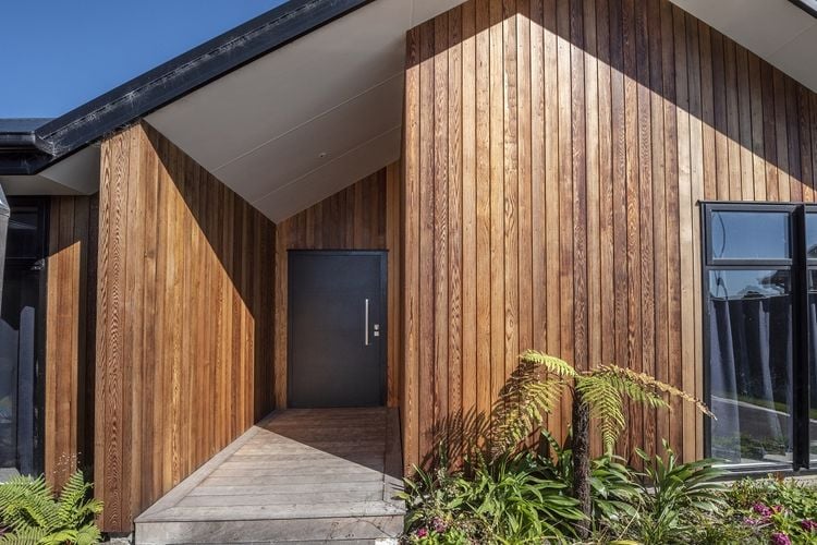 Exterior of a timber-clad house with a recessed entry and dark grey front door.