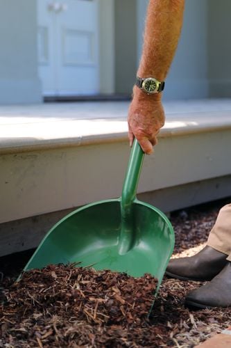 Person using large outdoor shovel to pick up wood chips