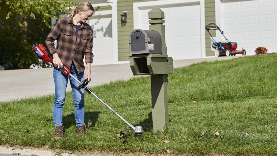 Person holding a trimmer and trimming the edges around a letterbox