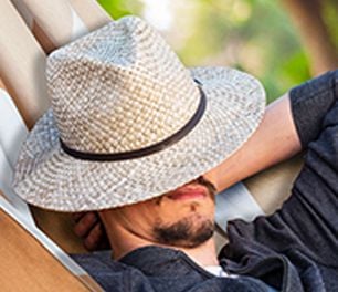 Closeup of a man with a straw hat pulled over his eyes reclining in a hammock