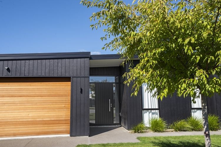 Front of black painted timber house with garage and tree