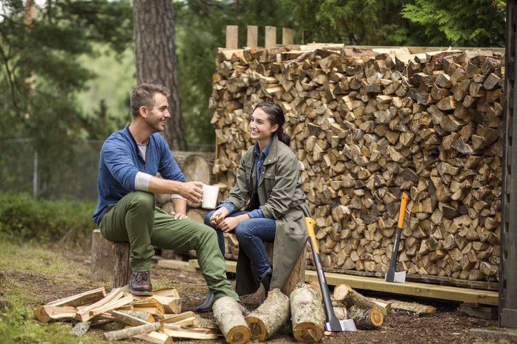 Couple sitting on wood blocks next to a pile of chopped firewood