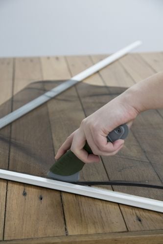 Person using tool to feed fly wire/screen in a frame