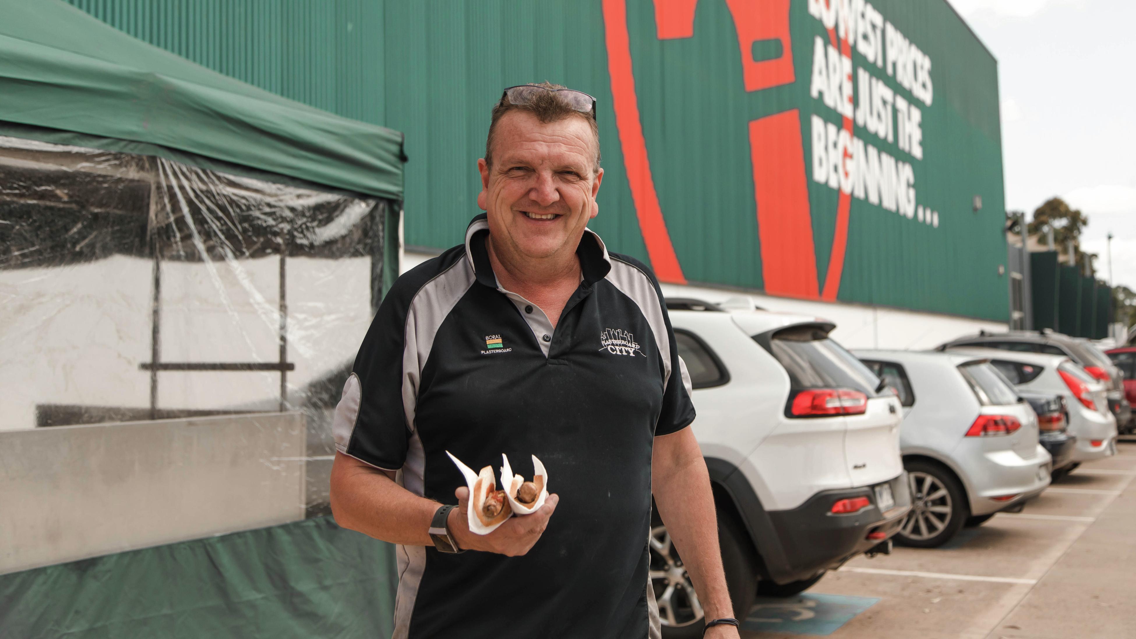 A person holding a sausage in bread out the front of a Bunnings store