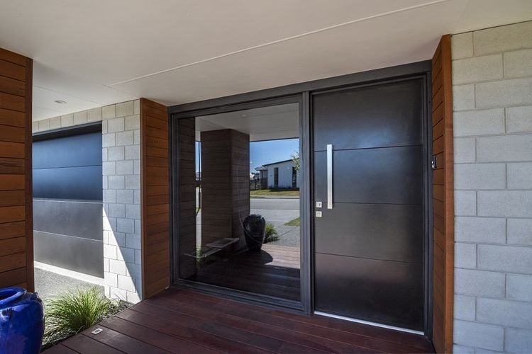 Covered entry to a grey brick house with a black front door.